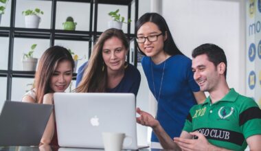 four people watching on white MacBook on top of glass-top table